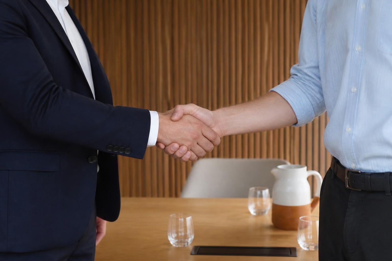 Two people shake hands next to a meeting table